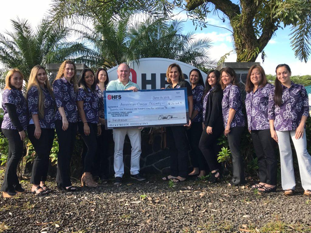 HFS staff members in Keaau pose for a photo in front of the HFS sign with Lee Lord and Sarah Luchenbill of the American Cancer Society. They are holding the large check presented from HFS for the Annual Fundraiser donation.