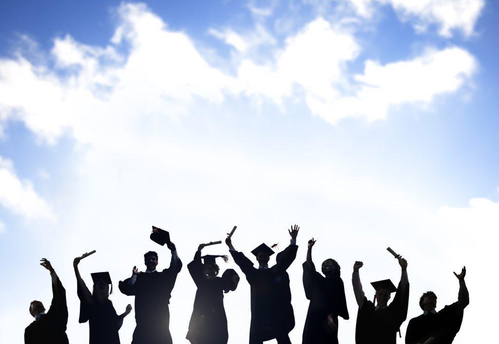 silhouettes of graduates celebrating with a sky background