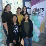 students stand in front of a welcome sign and balloons at the entrance to their classroom