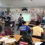 a staff member stands at the front of the classroom talking to students about the Reality Fair Workshop instructions