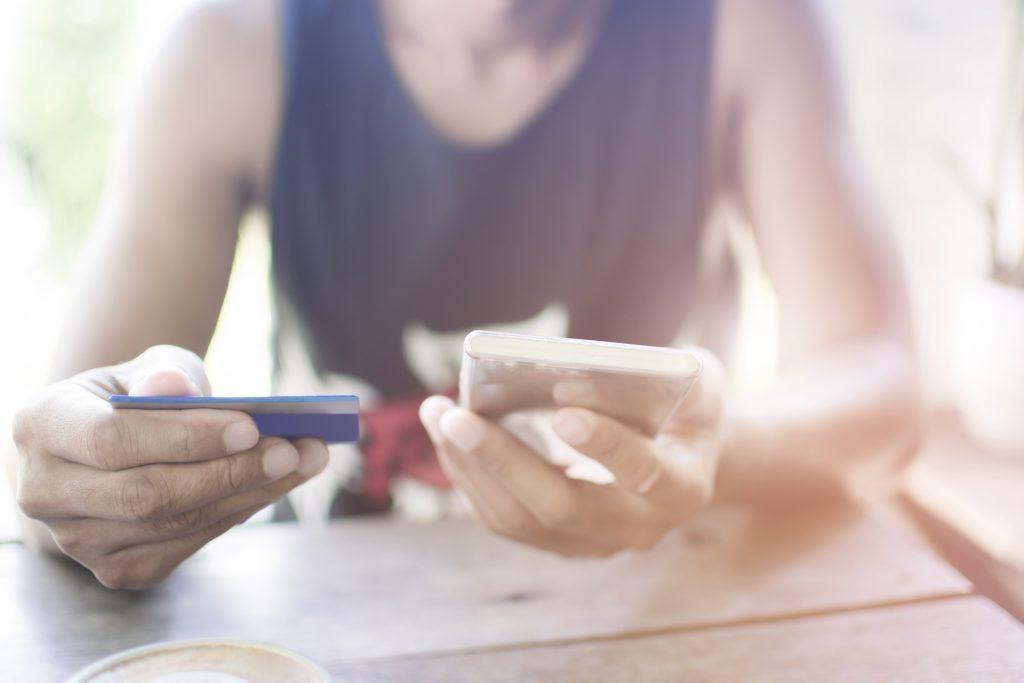 Soft focus Hipster Asian manâ€™s hands using smart phone and holding a credit card for online shopping while sitting at the wooden table in coffee shop