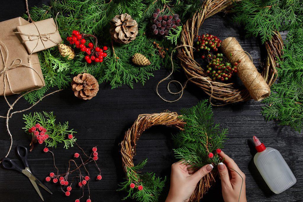Top view of female hands make a Christmas wreath. Packed gifts and scrolls