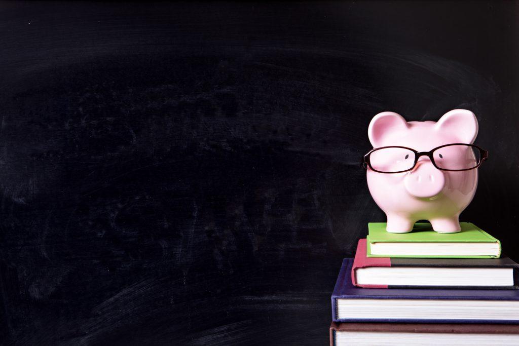 piggy bank with glasses on a stack of books infront of a chalkboard