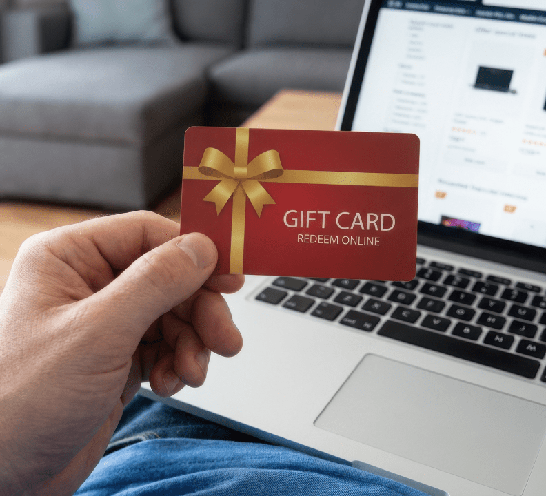 person holding gift card by laptop